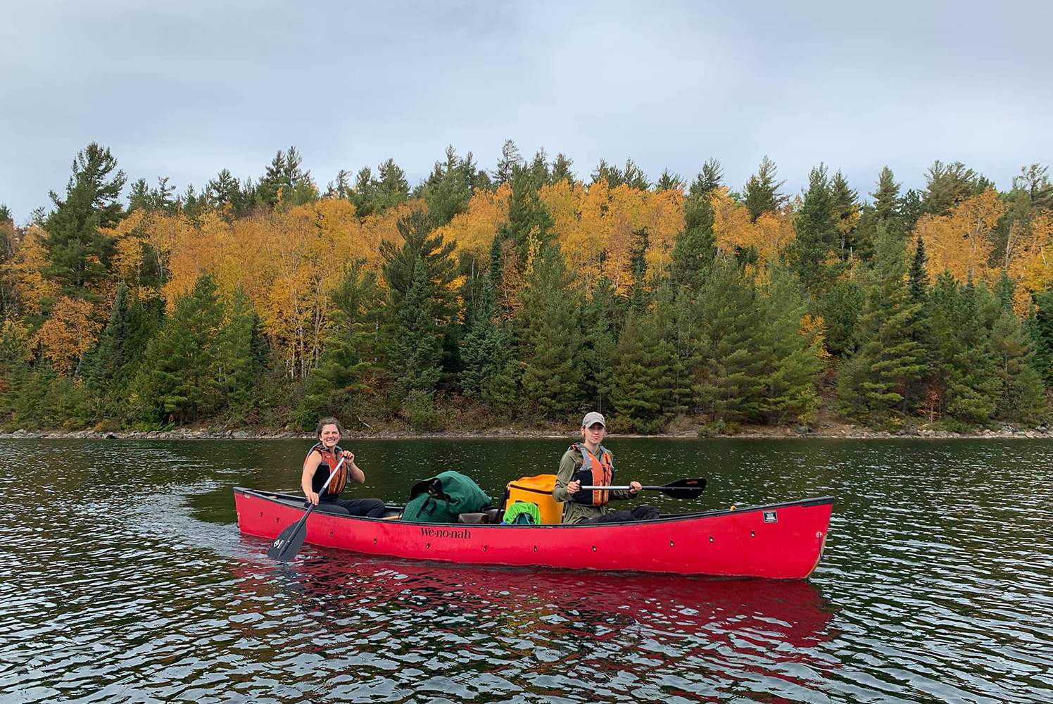 two students, male and female, on a red canoe on the lake with trees in the background