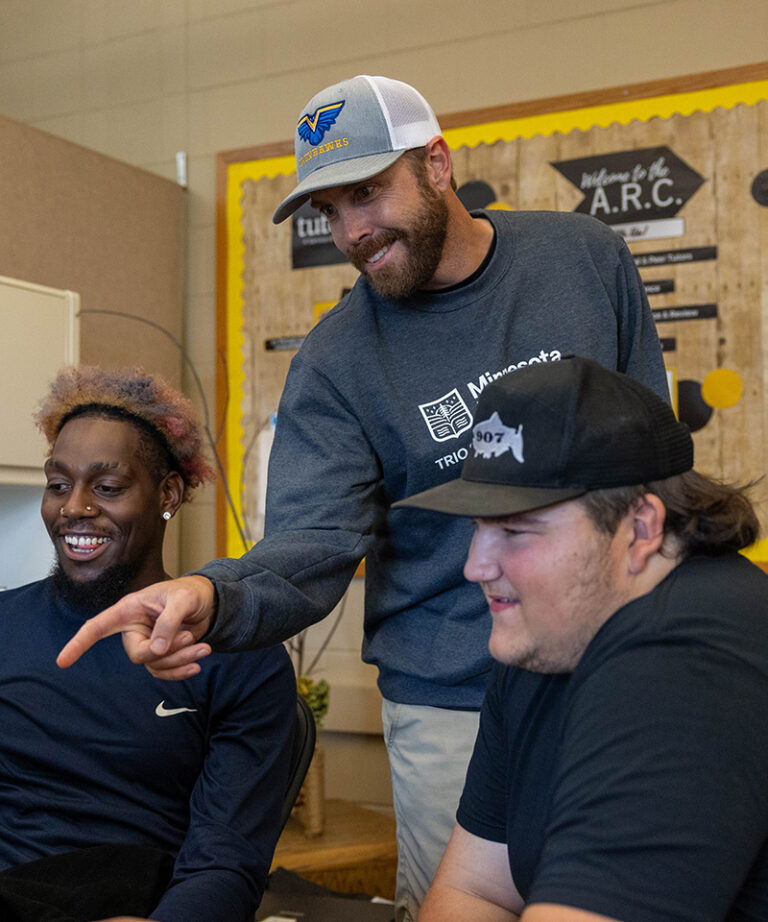 3 men, one male smiling, one with a hat on pointing, and another with a hat on smiling