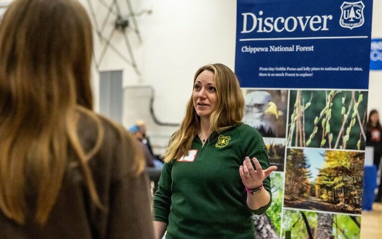 caucasian woman talking in front of a united states forest service banner