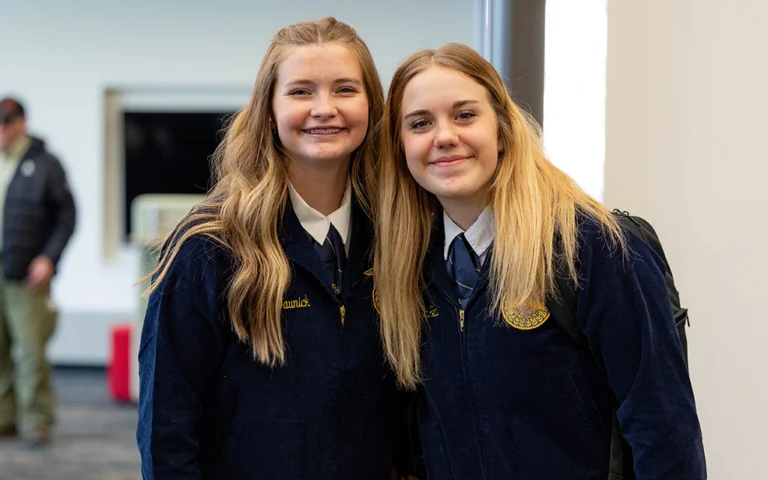 two girls with blonde hair smiling wearing dark blue jackets