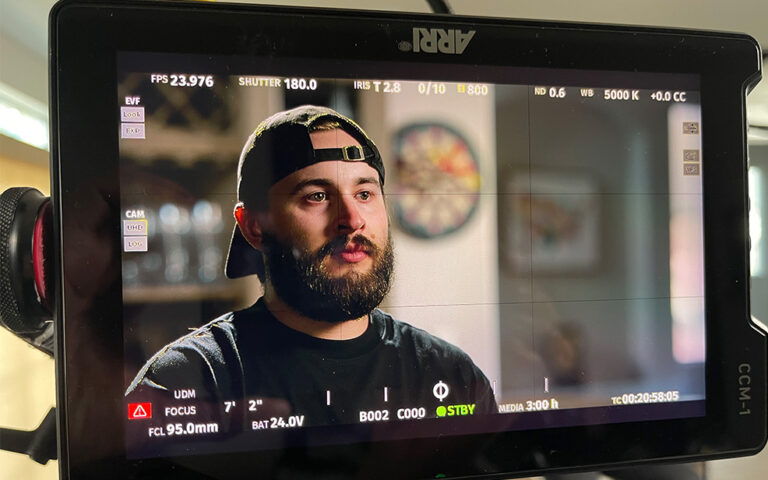 Close-up of a video monitor showing Nick Perronteau, wearing a backwards cap and speaking on camera during an interview setup.
