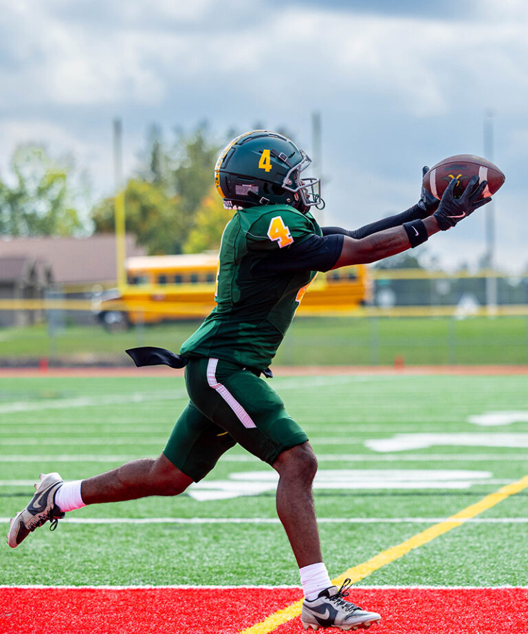 male football athlete catching a the ball in front of him in the endzone for a touchdown