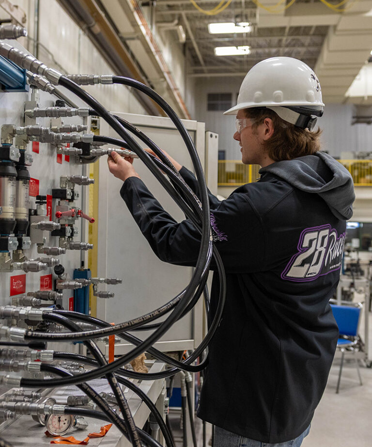 caucasian male student with white hard hat working on an electrical board