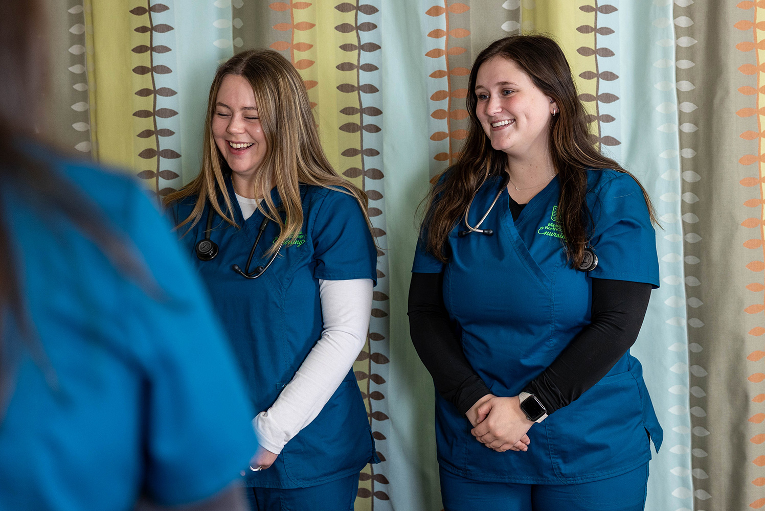 two nursing students smiling while wearing scrubs