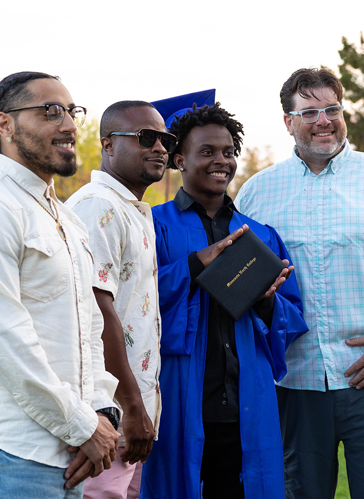three males around one graduate smiling, holding the diploma up