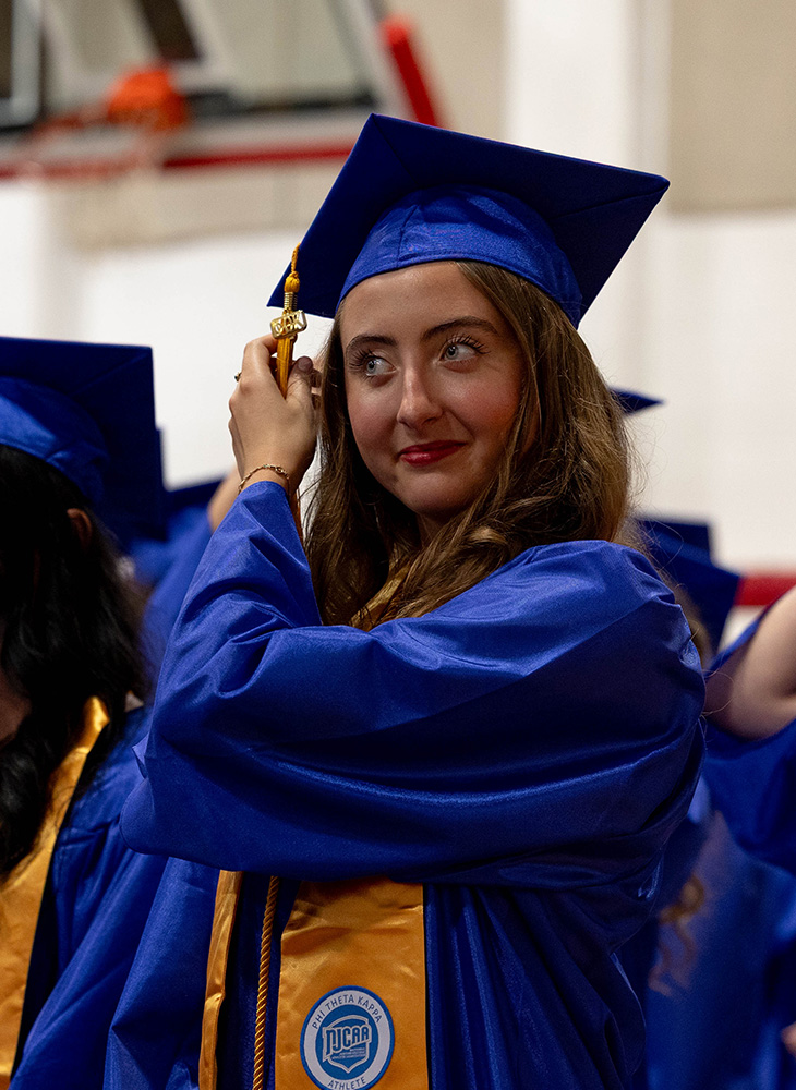 female student with blue cap and gown going to turn her tassel