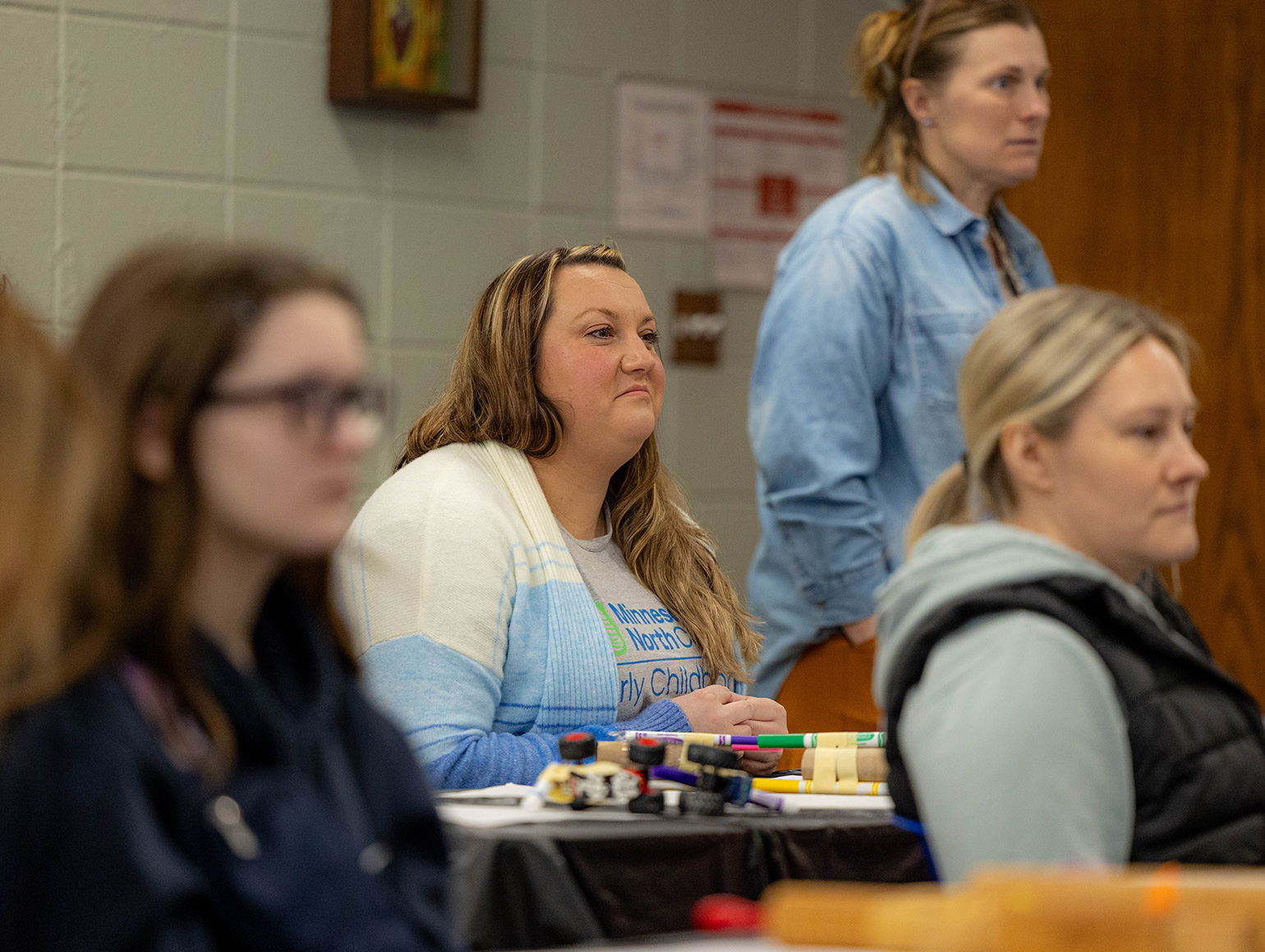 girl with long blonde hair and a cardigan on with toys in front of her sitting and listening